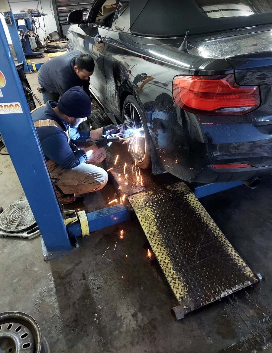 Llantera Del Norte technicians working on a vehicle raised on the lift at 606 Peoria St in Aurora, Colorado, with the wheel removed for brake and undercarriage service / Técnicos de Llantera Del Norte trabajando en un vehículo levantado en el elevador, en el 606 de Peoria St en Aurora, Colorado, con la rueda quitada para servicio de frenos