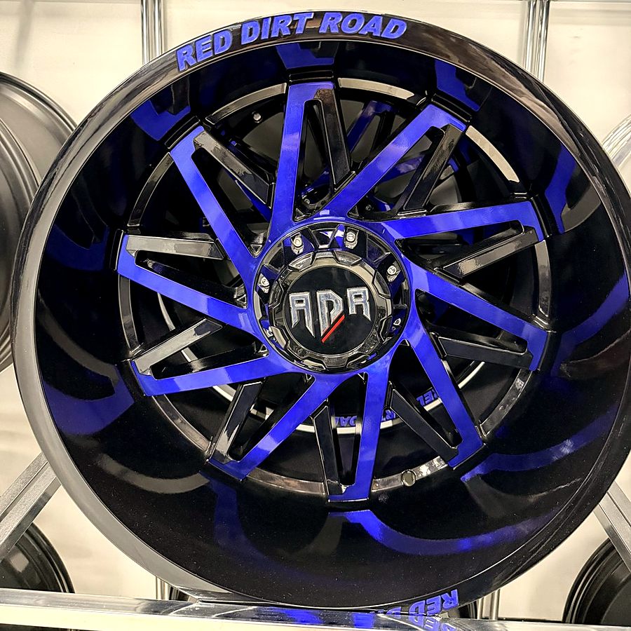 Red Dirt Road gloss black truck wheel with blue accent spokes on the wheel wall at Llantera Del Norte INC, 606 Peoria St, Aurora, Colorado / Rin de troca Red Dirt Road negro brillante con rayos de acento azul en Llantera Del Norte INC en Aurora, Colorado